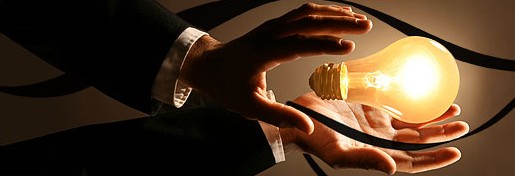 Dłonie trzymające świecącą żarówkę na ciemnym tle